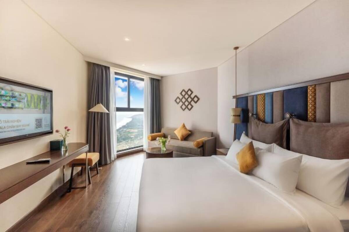 Ein Hotelzimmer mit einem großen Bett, einem Schreibtisch, einem Sessel, einem Fernseher und Blick ins Freie.