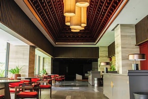 A hotel lobby with a reception desk, seating area, and a modern ceiling design. - Apec Mandala Chambay Mui Ne - Oceanic Studio (Phan Thiet)