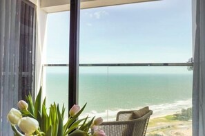A balcony with a view of the ocean, a wicker chair, and a vase of flowers. - Apec Mandala Chambay Mui Ne - Oceanic Studio (Phan Thiet)