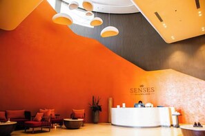 A reception area with a curved reception desk, seating area with sofas, and a large potted plant. - Apec Mandala Chambay Mui Ne - Oceanic Studio (Phan Thiet)