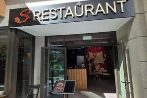 Entrada de un restaurante con puerta de vidrio, un atril para el menú y un letrero en la parte superior.