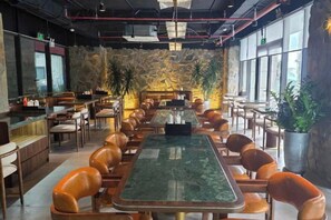 A restaurant with a long communal table surrounded by chairs, a bar area, and large windows. - Apec Mandala Chambay Mui Ne - Oceanic Studio (Phan Thiet)