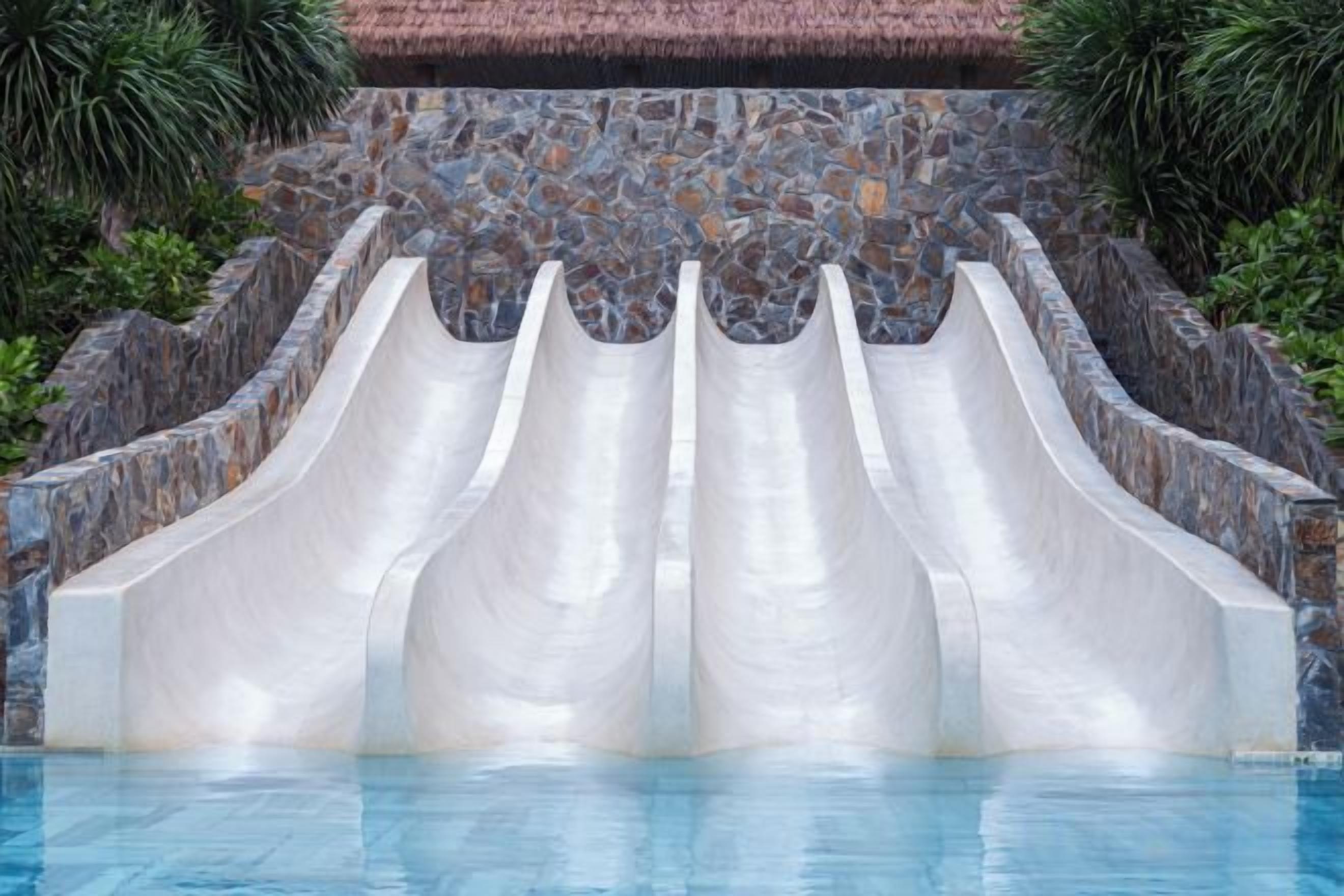 A pool with three water slides against a stone wall backdrop.