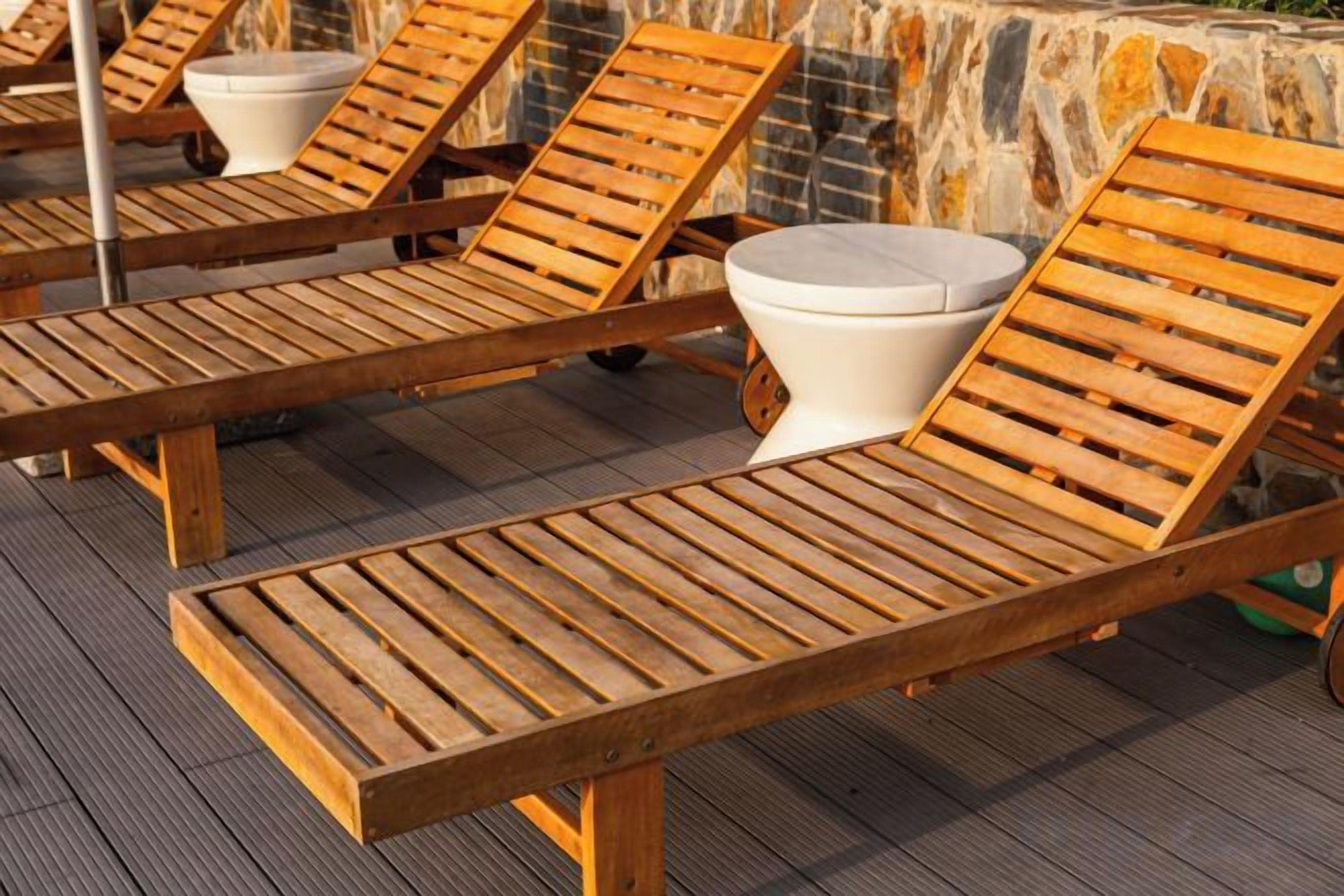 Wooden lounge chairs with white cushions and a stone wall in the background.