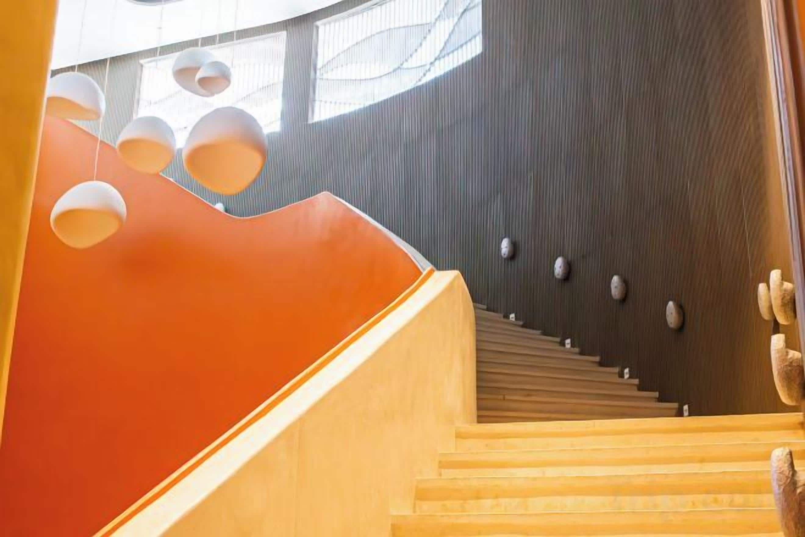 A staircase with wooden steps and a curved railing, leading to a dark wall with circular light fixtures.