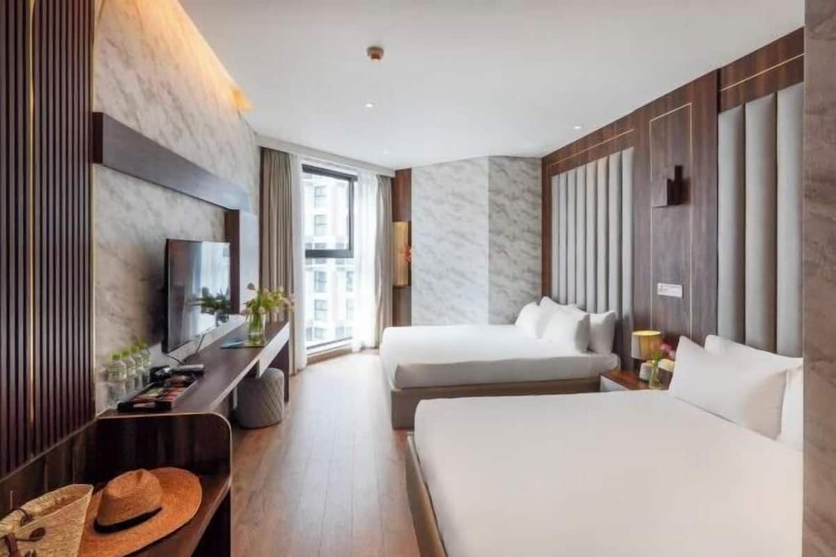 Ein modernes Hotelzimmer mit zwei Betten, einem Fernseher, einem Schreibtisch mit Computer und einem großen Fenster.