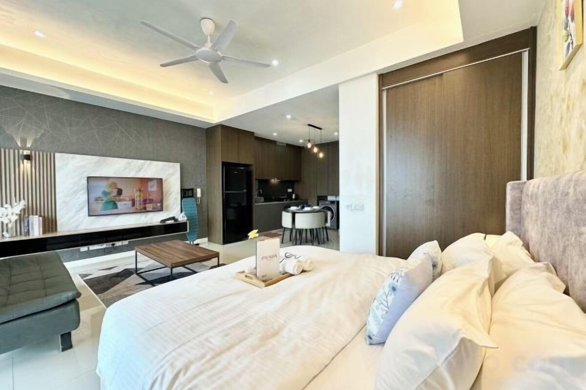 Une chambre moderne avec un grand lit, une télévision, un coin repas et une cuisine en arrière-plan.