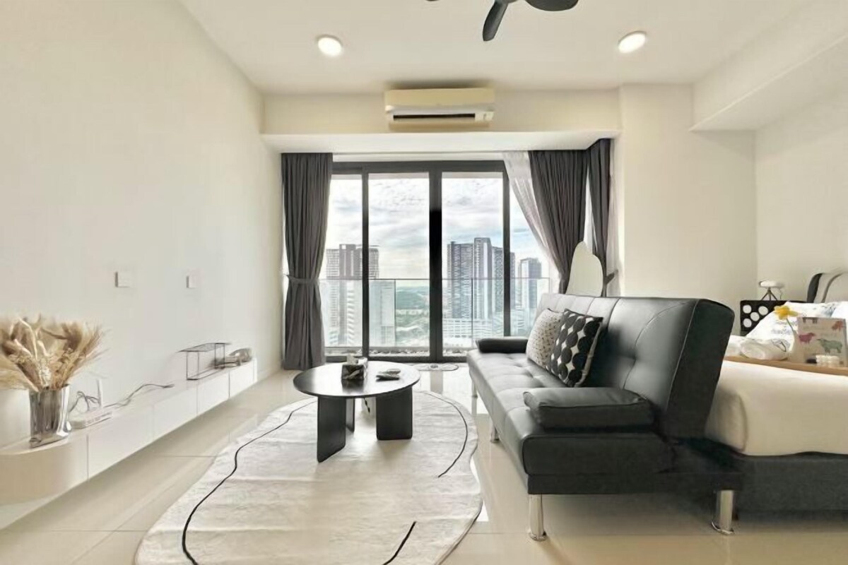 Una sala de estar moderna con un sofá, una mesa de centro y vistas a un paisaje urbano a través de amplios ventanales.