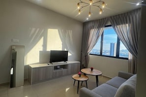 A modern living room with a sofa, two small tables, a TV on a wooden cabinet, and a large window with curtains.