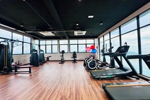 Een fitnessruimte met trainingsapparatuur, grote ramen en een houten vloer.