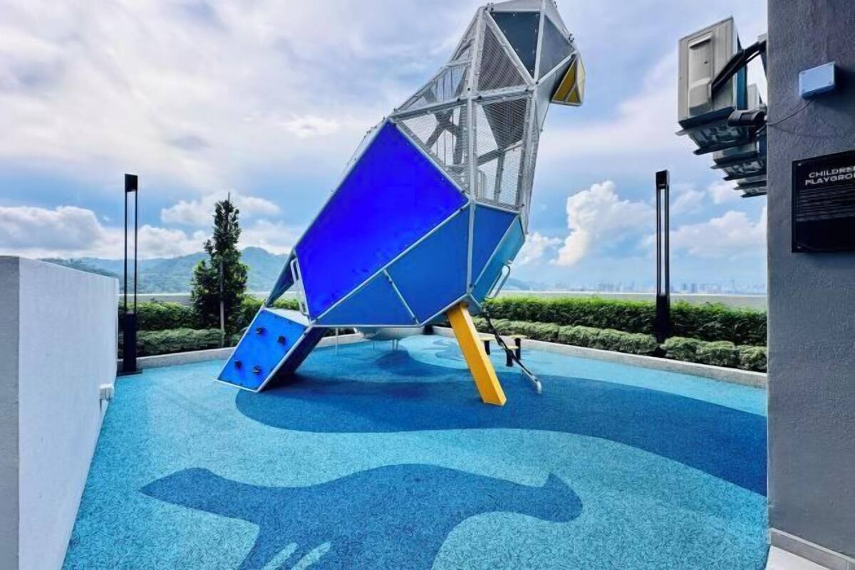 A blue and white geometric structure in an outdoor area with a blue floor, surrounded by greenery and a clear sky.