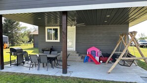 A covered patio with a table and chairs, a playhouse, and a swing set. - Superb 4-bedroom house with AC in Whitney (Whitney)