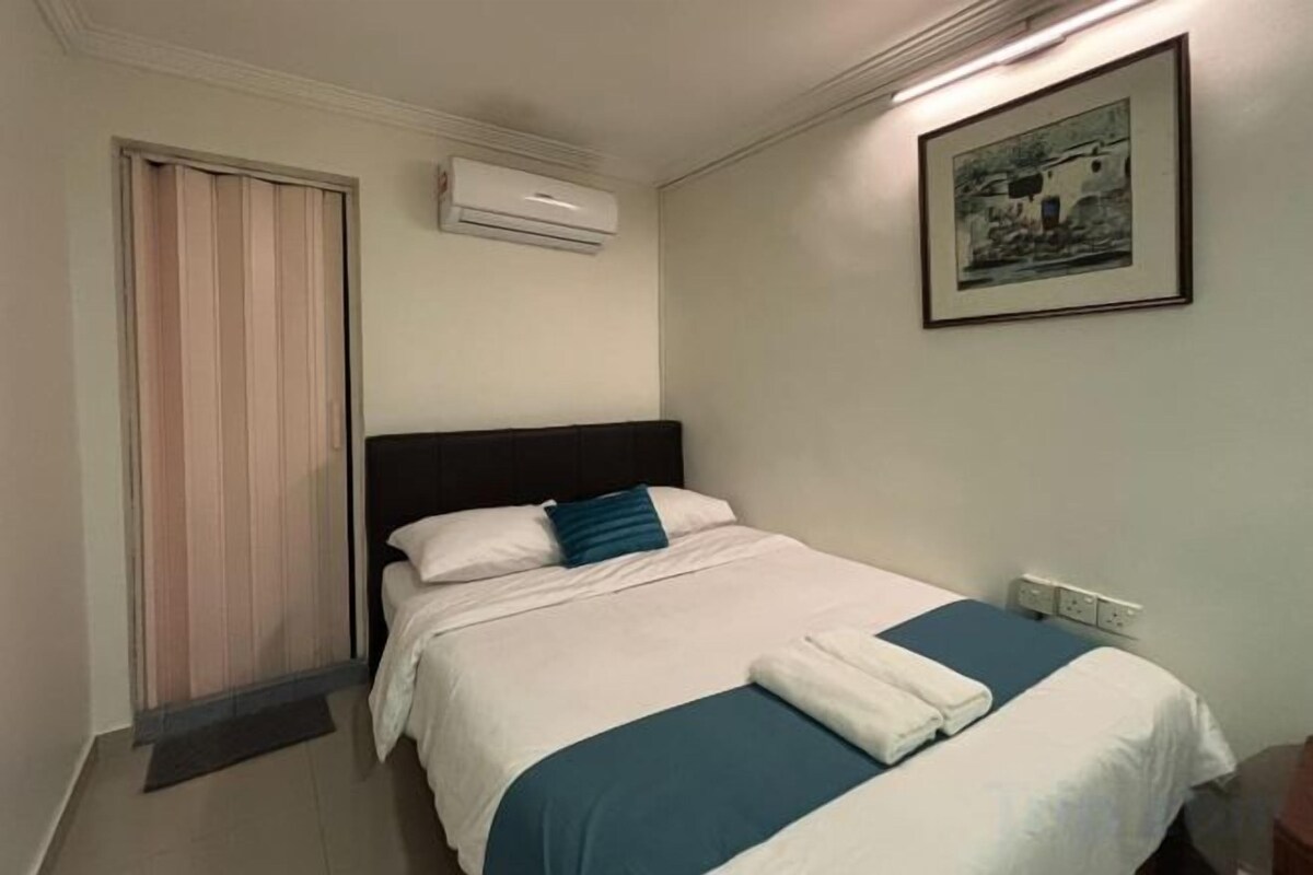 A hotel room with a bed, a window with blinds, an air conditioning unit, and a framed picture on the wall.