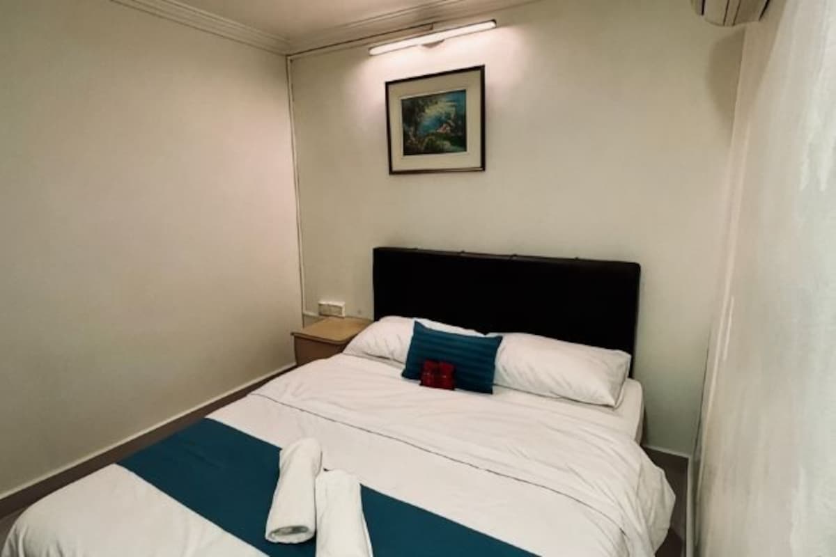 A hotel room with a bed, a nightstand, a painting on the wall, and a window with curtains.