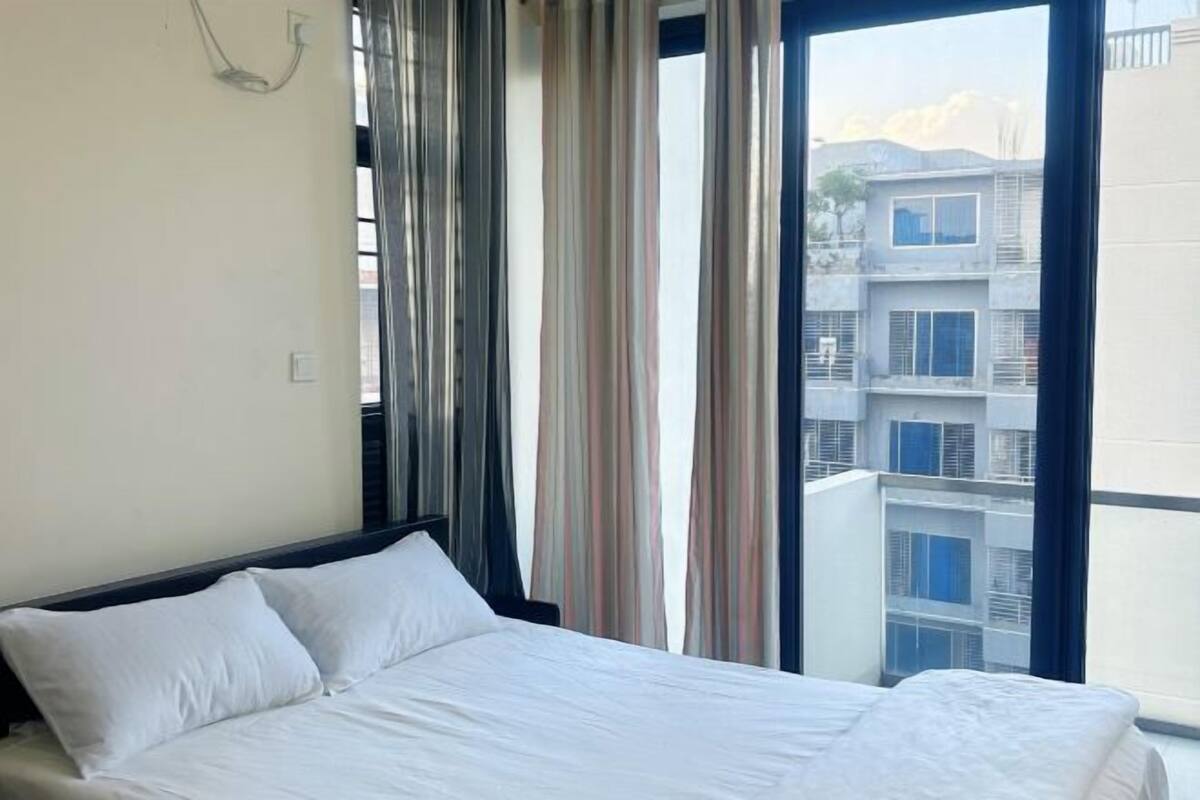 Ein Hotelzimmer mit einem großen Bett, einem Fenster mit Vorhängen und Blick auf ein Gebäude.