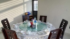 A round glass table with a lace tablecloth, surrounded by wooden chairs.