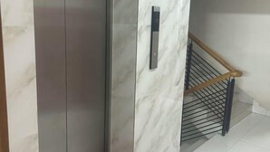 A marble elevator door with a handrail and a metal staircase with a wooden handrail.