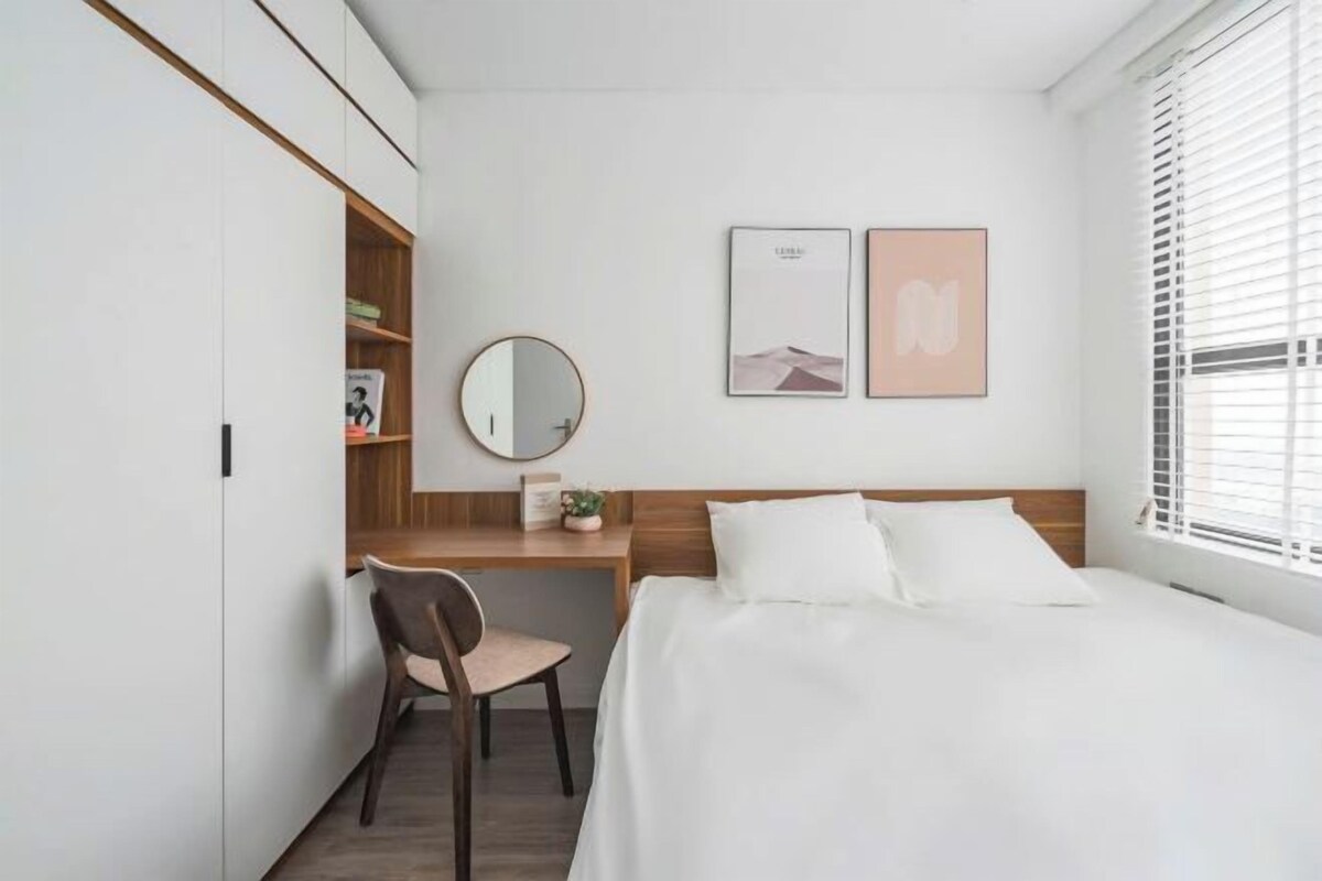 A bedroom with a bed, a desk, a chair, a mirror, and two framed pictures on the wall.
