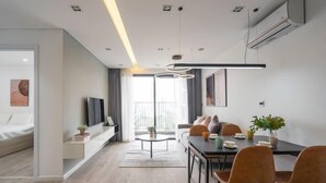 Ein modernes Wohnzimmer mit einer Couch, einem Esstisch mit Stühlen, einem Fernseher und einem großen Fenster mit Vorhängen.