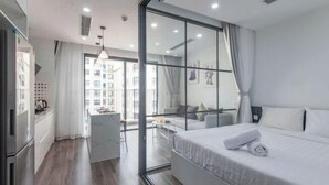 Ein modernes Hotelzimmer mit Bett, Schreibtisch, Sessel und Blick auf die Stadt durch große Fenster.