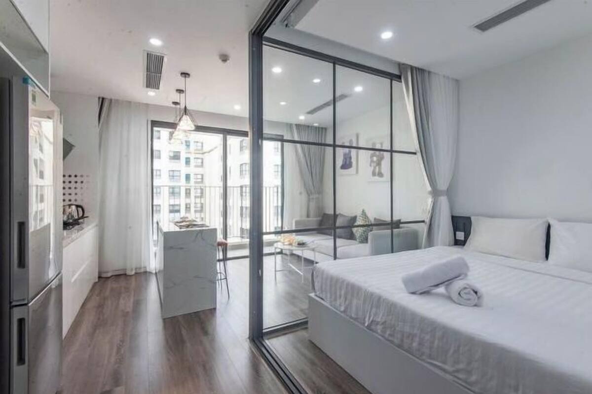 Ein modernes Hotelzimmer mit Bett, Schreibtisch, Sessel und Blick auf die Stadt durch große Fenster.