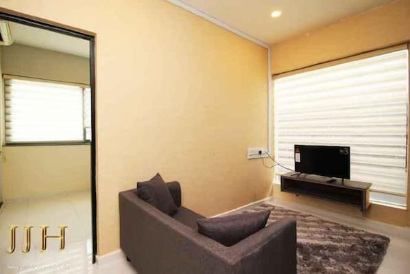 A modern living room with a sofa, a flat-screen TV, and a large window with blinds. - JJH Serviced Apartments Near Serangoon MRT (Singapore)