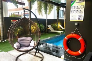 A hanging chair by a poolside, a life ring on the wall, and a glimpse of the pool area. - JJH Serviced Apartments Near Serangoon MRT (Singapore)