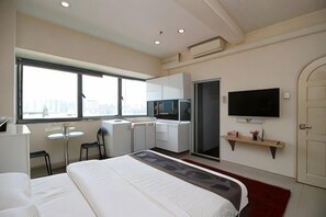 A modern hotel room with a large bed, a desk, a TV, and a window with a city view.