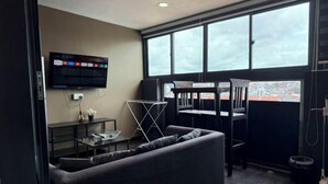 A modern room with a sofa, a TV mounted on the wall, a dining table, and a view through large windows. - JJH Serviced Apartments Near Serangoon MRT (Singapore)