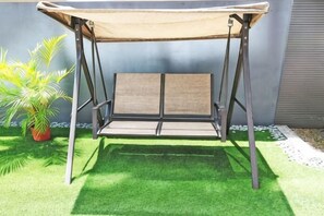 A swing with a canopy, positioned on artificial grass, next to a wall and a potted plant. - JJH Serviced Apartments Near Serangoon MRT (Singapore)