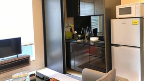 A compact kitchen with a microwave, refrigerator, and a flat-screen TV. - JJH Serviced Apartments Near Serangoon MRT (Singapore)
