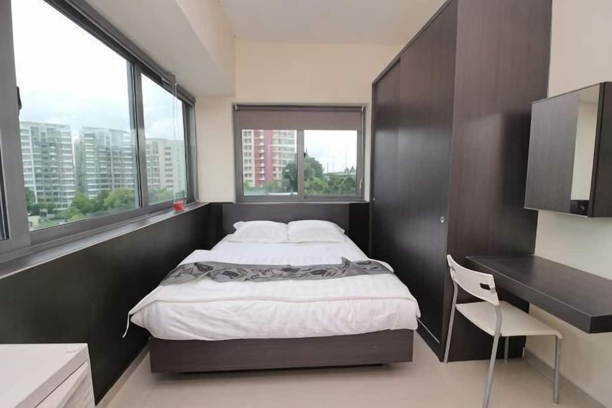 A bedroom with a bed, a desk, a chair, and a large window.
