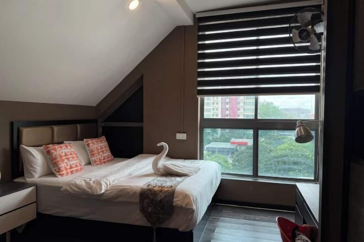 A bedroom with a bed, pillows, a swan decoration, a window with blinds, and a fan.