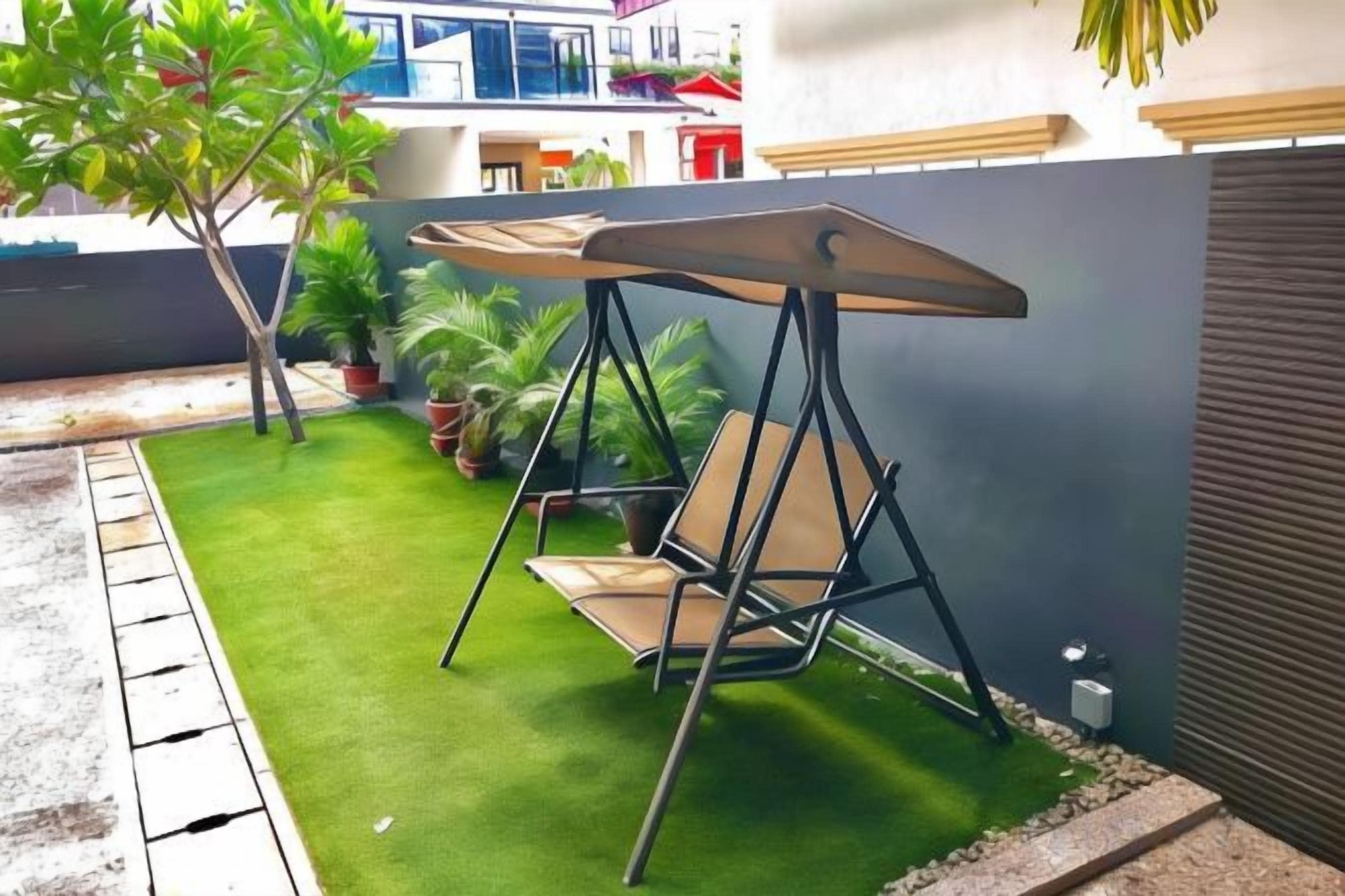 A patio with a swing chair, green artificial grass, and potted plants.