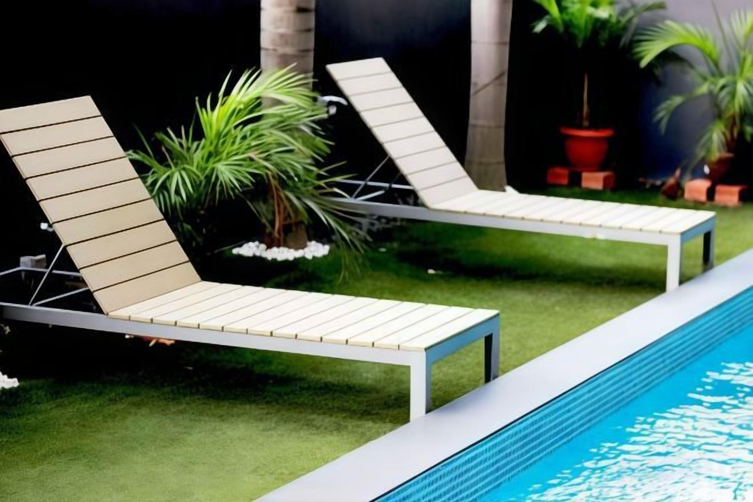 Two lounge chairs by a poolside with artificial grass and potted plants.