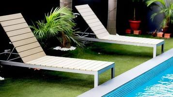 Two lounge chairs by a poolside with artificial grass and potted plants.