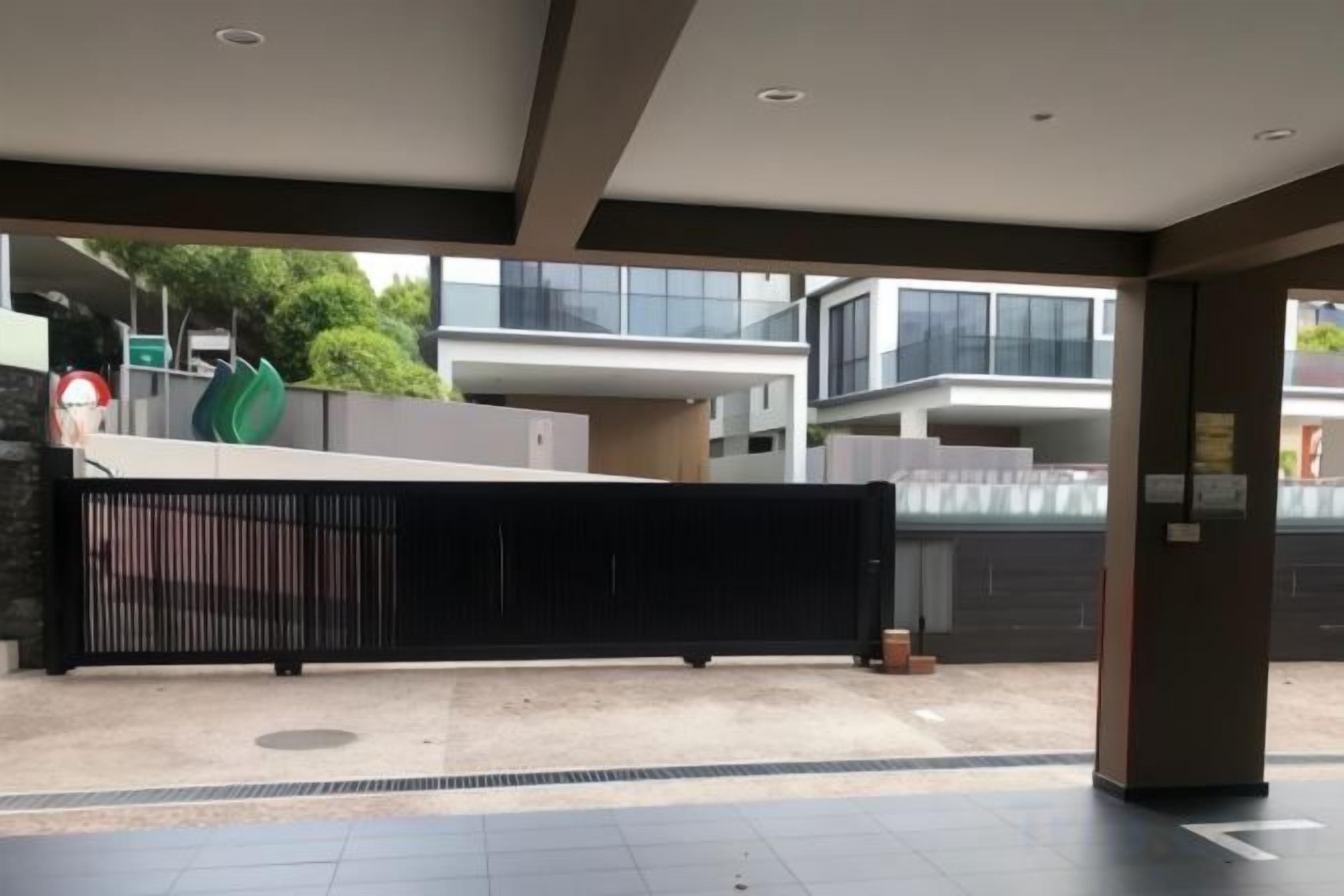 A modern building entrance with a black gate, a paved area, and a view of a residential building in the background.