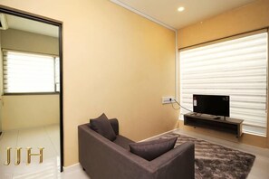 Ein Wohnzimmer mit einer Couch, einem Flachbildfernseher und einem Fenster mit Jalousien.