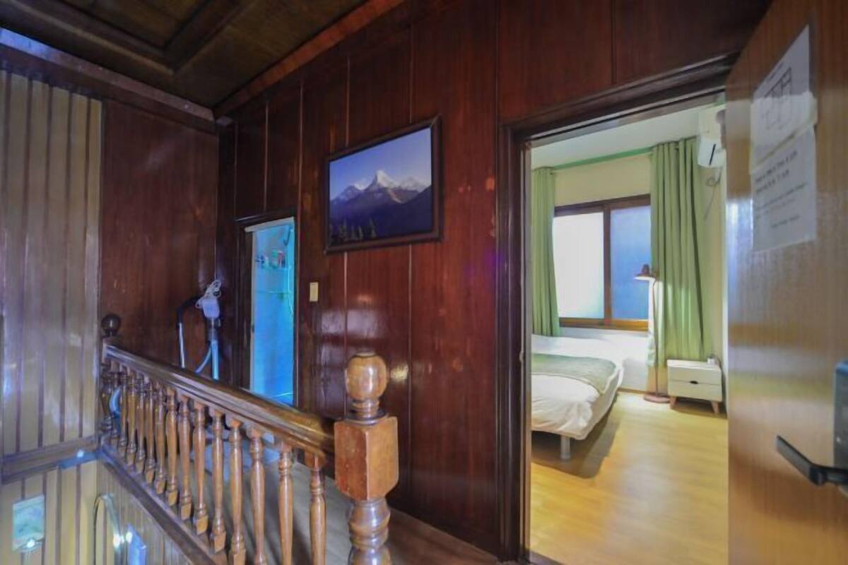 Una escalera de madera que lleva a una habitación con una cama, una ventana con cortinas y un cuadro en la pared.