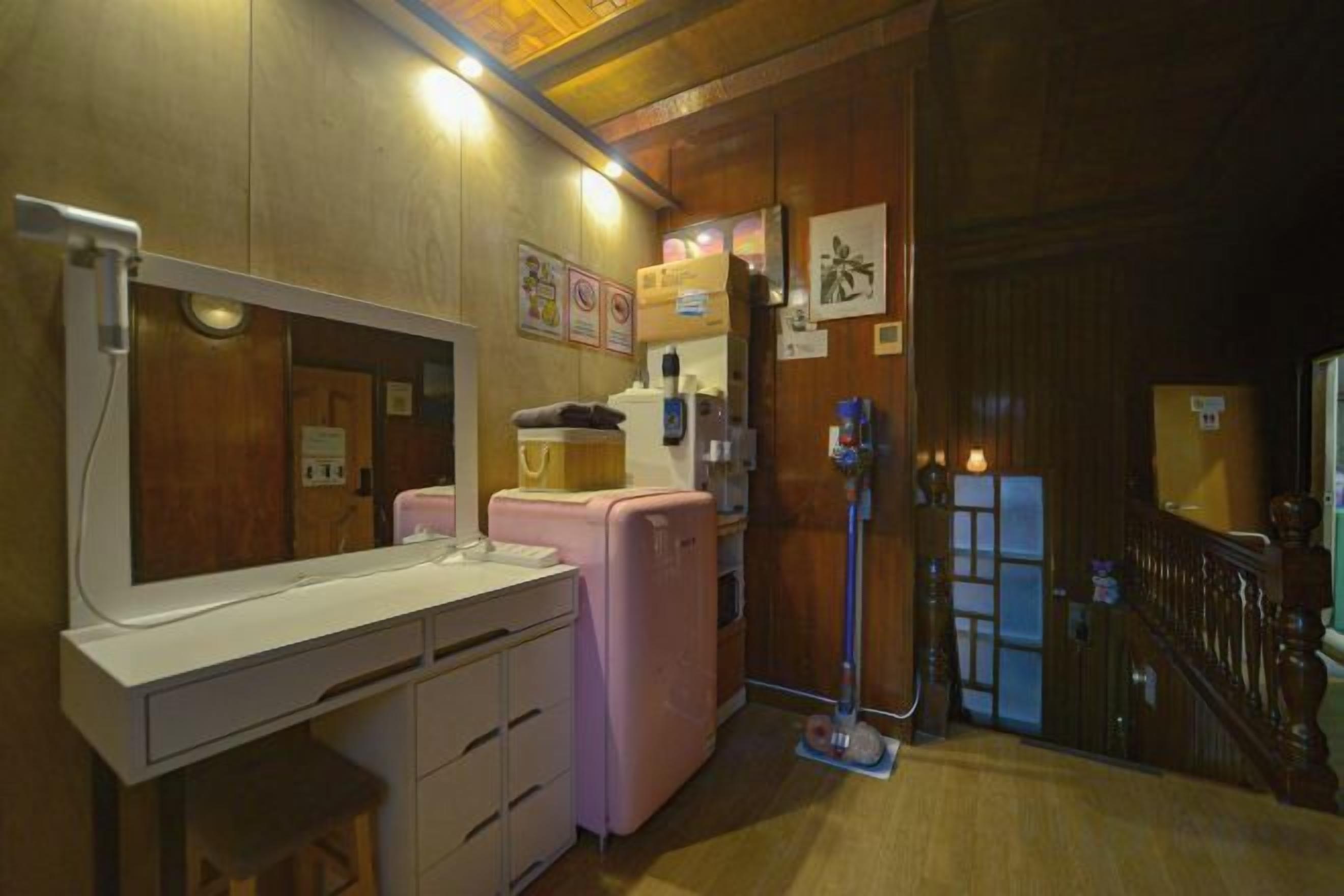 A compact room with a kitchenette, a mirror, a small sink, and a door leading to another room.