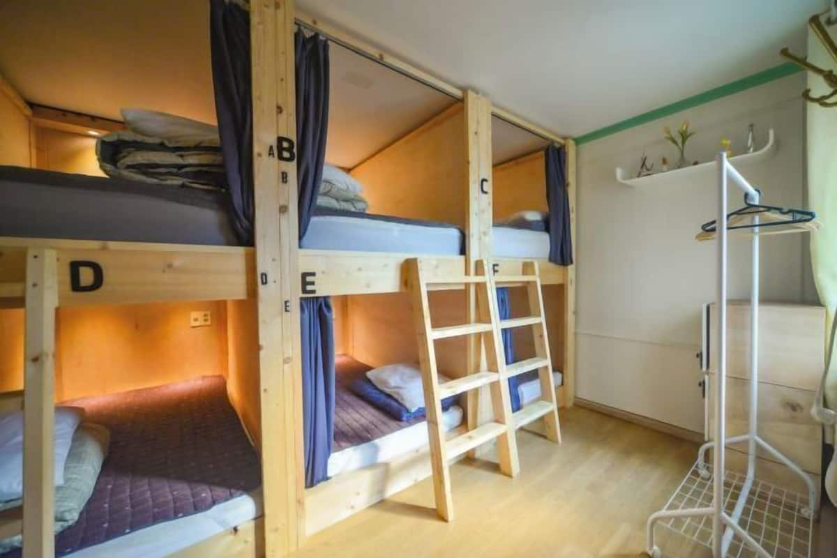 Habitación con literas, una escalera, un estante metálico blanco y un estante fijado a la pared.