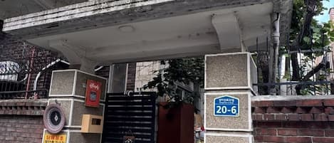 Une entrée fermée par un portail, avec une enseigne bleue, un mur de briques et une structure en béton au-dessus.