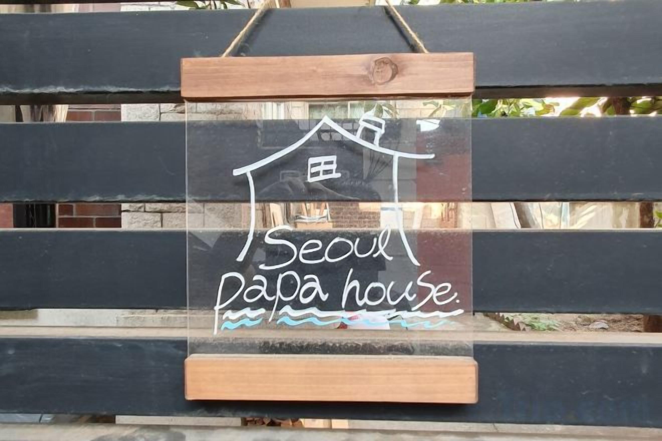 Et skilt med en hus-silhuet og teksten 'Seoul papa house' mod en træbaggrund.