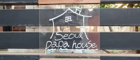 Et skilt med en hus-silhuet og teksten 'Seoul papa house' mod en træbaggrund.