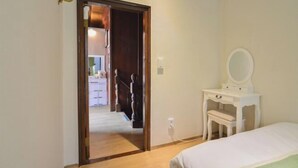 Une chambre à coucher avec un lit, une commode blanche avec un miroir et une porte donnant sur un couloir.