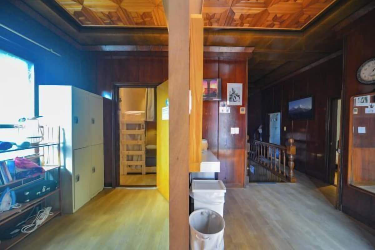 Un interior de madera con un pasillo que lleva a una puerta, un cubo de basura y un reloj en la pared.