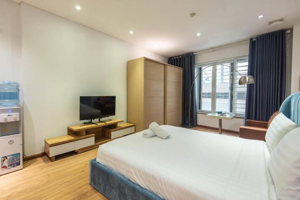 Habitación de hotel con cama, televisor, dispensador de agua, escritorio y ventana con cortinas.