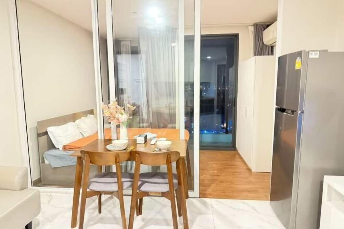 A dining area with a table and chairs, a sofa, and a refrigerator.