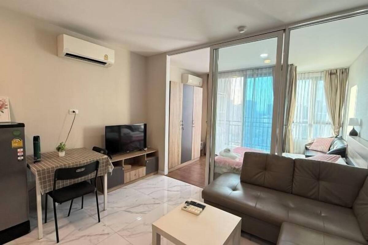 A living room with a sofa, a TV, a small table, and a balcony with curtains.