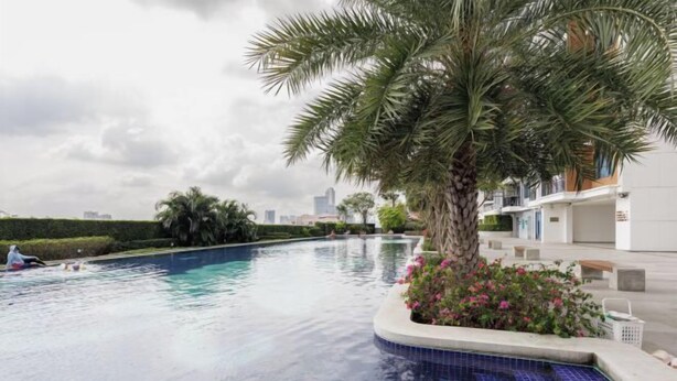 A swimming pool with a tiled edge, surrounded by a low wall and a palm tree. - Artisan Ratchada Apartment Bangkok, Thailand (Bangkok)